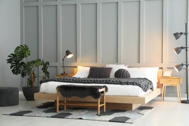 Photo of Stylish bedroom interior with comfortable bed, lamps and houseplant