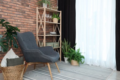 Shelving unit, green houseplants, armchair, pillows and elegant curtain in room. Interior design