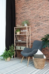 Photo of Shelving unit, green houseplants, armchair, pillows and elegant curtain in room. Interior design