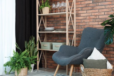 Shelving unit, green houseplants, armchair, pillows and elegant curtain in room. Interior design