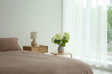 Photo of Stylish bedroom interior with comfortable bed, bouquet of flowers and bedside table