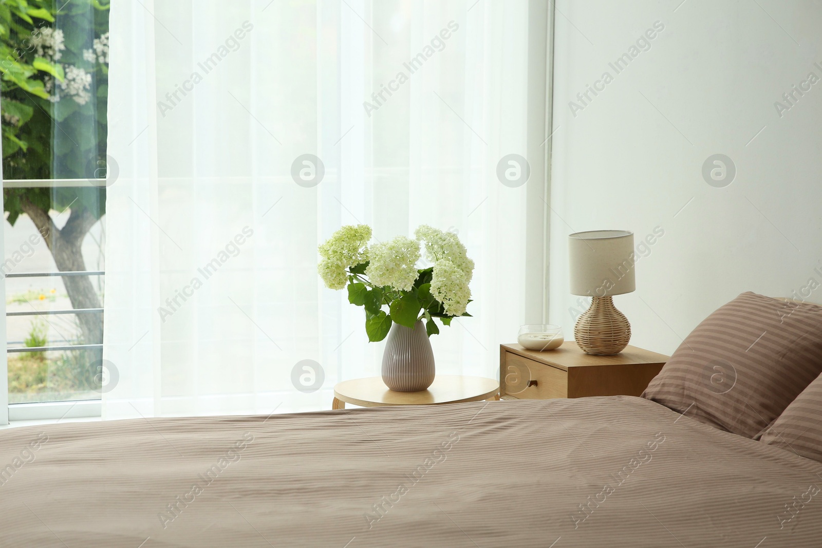 Photo of Stylish bedroom interior with comfortable bed, bouquet of flowers and bedside table