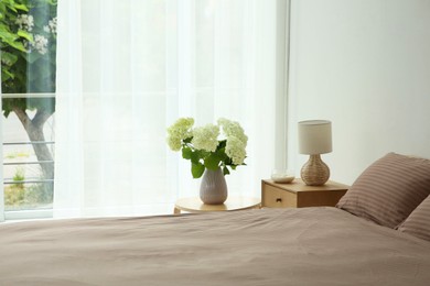 Stylish bedroom interior with comfortable bed, bouquet of flowers and bedside table