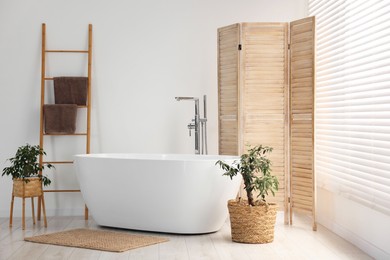 Photo of Wooden folding screen, bathtub and green houseplants in bathroom