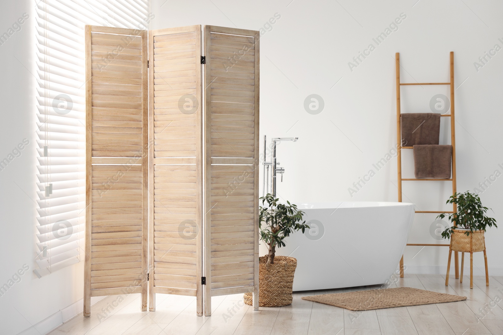 Photo of Wooden folding screen, bathtub and green houseplants in bathroom