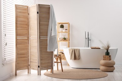 Wooden folding screen, bathtub, chair and rack in bathroom