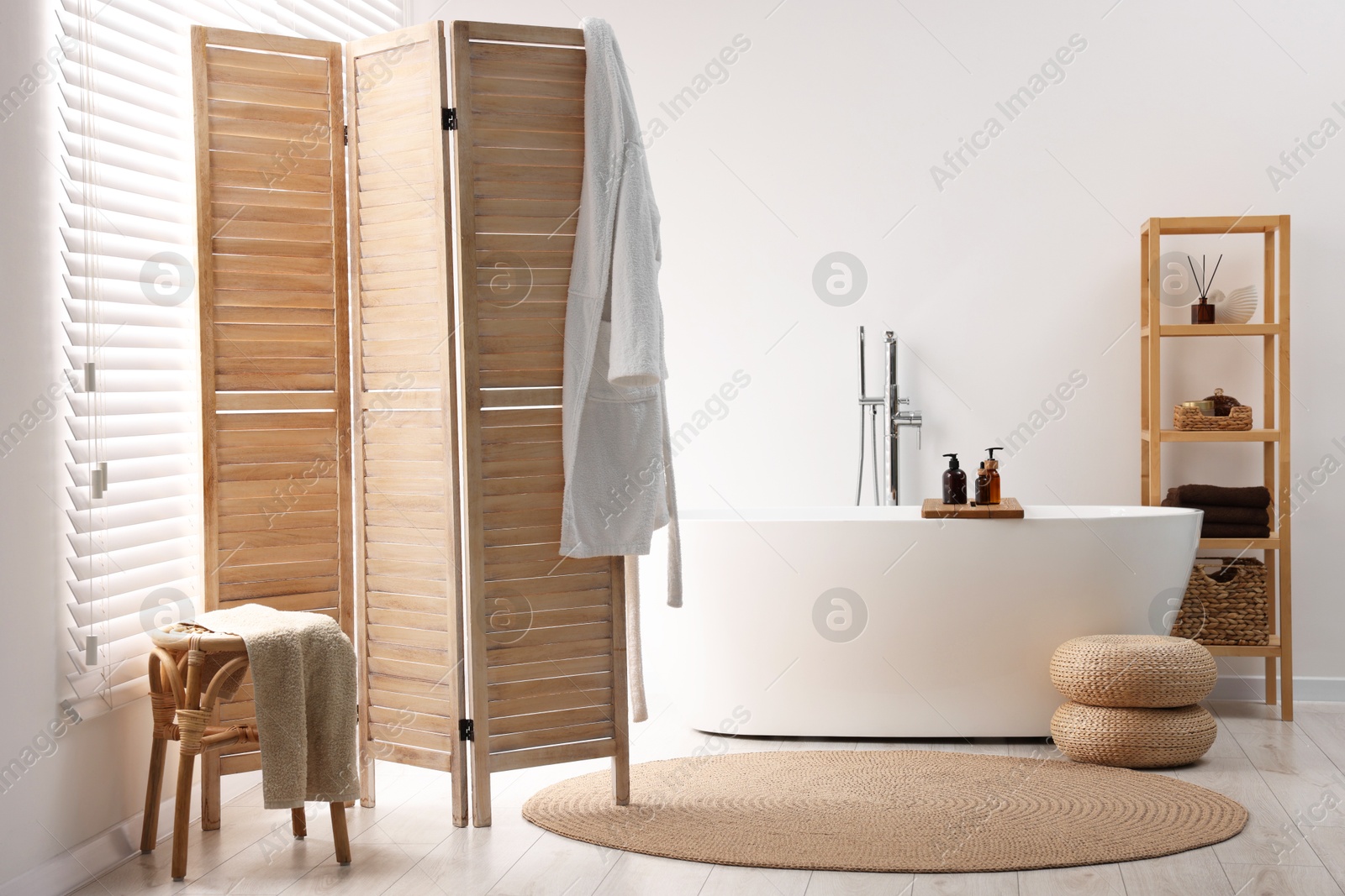 Photo of Wooden folding screen, bathtub, chair and rack in bathroom