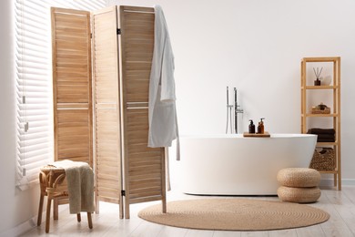 Photo of Wooden folding screen, bathtub, chair and rack in bathroom