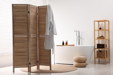 Photo of Wooden folding screen, bathtub and rack in bathroom