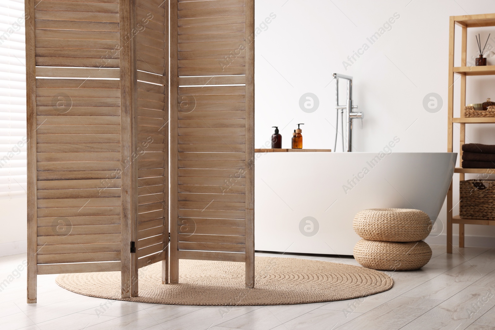 Photo of Wooden folding screen, bathtub and rack in bathroom