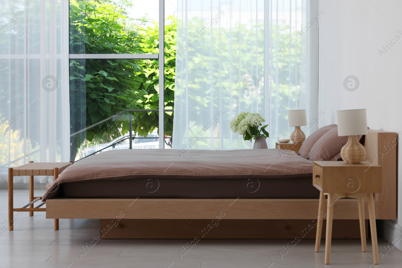 Photo of Stylish bedroom interior with large bed, bedside tables, lamps and ottoman