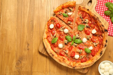 Tasty pizza with basil, mushrooms, mozzarella and tomato on wooden table, flat lay. Space for text