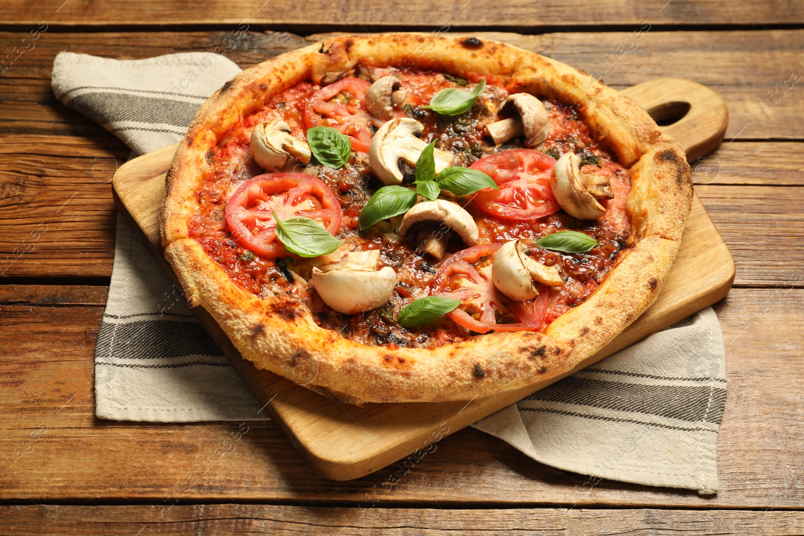 Photo of Tasty pizza with basil, mushrooms and tomato on wooden table