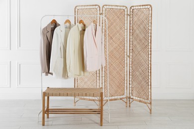 Folding screen, rack with clothes and storage bench near white wall indoors