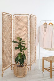 Photo of Folding screen, rack with clothes, storage bench and houseplant near white wall indoors