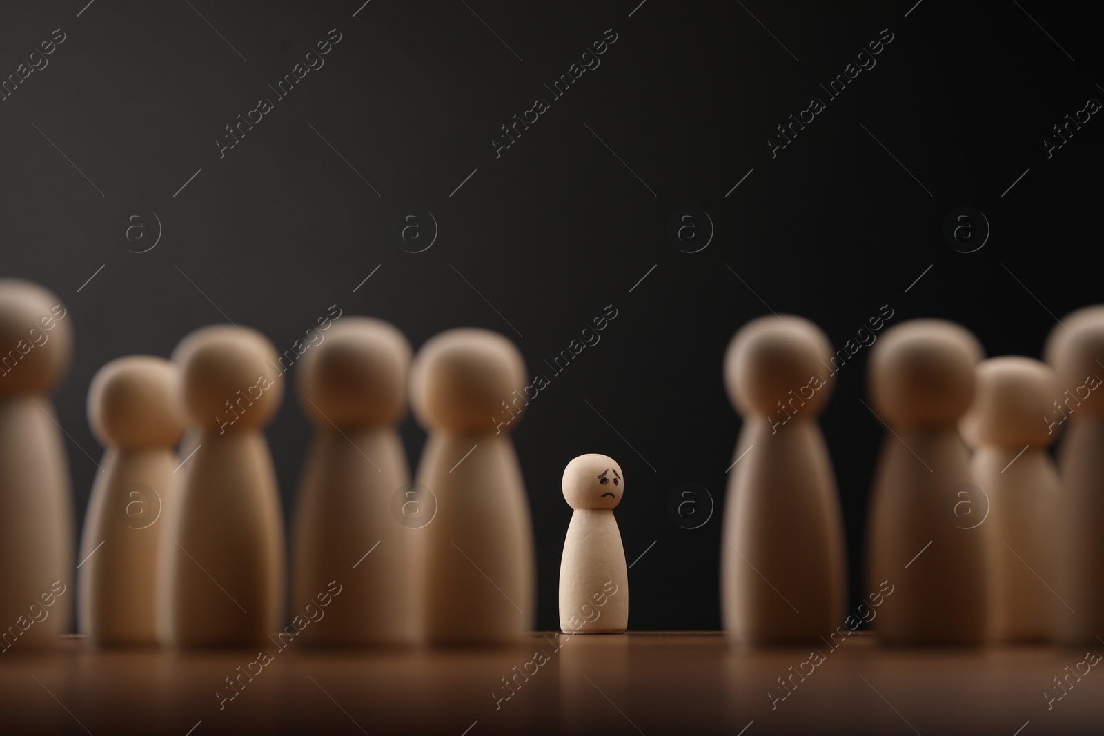 Photo of Loneliness concept. Human figure alone among others on wooden table