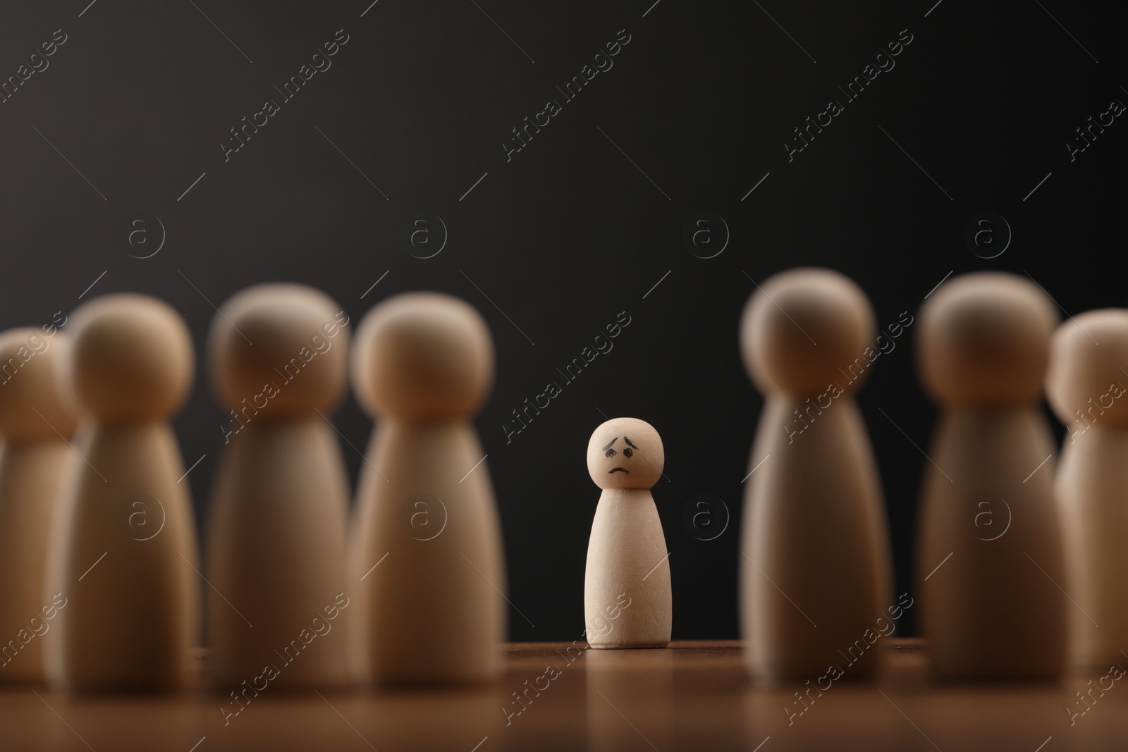 Photo of Loneliness concept. Human figure alone among others on wooden table