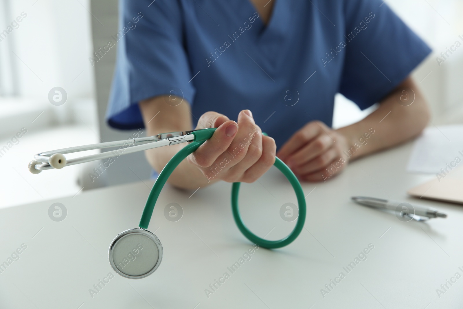 Photo of Doctor with stethoscope at white table in hospital, closeup