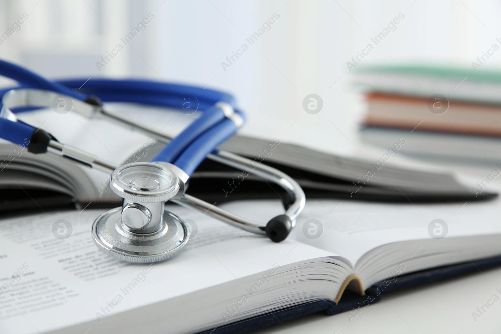 Photo of One medical stethoscope and books on white table, closeup