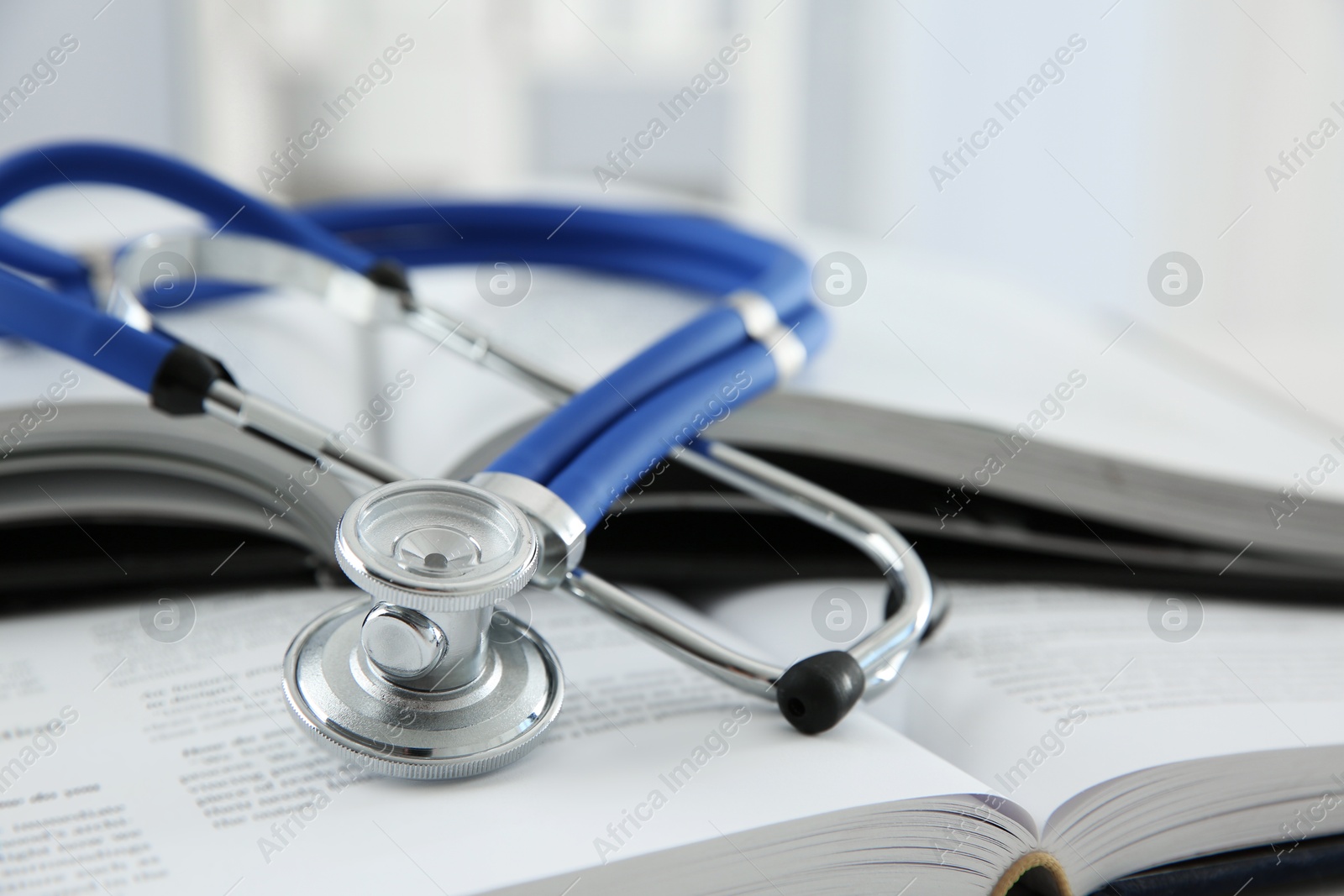 Photo of One medical stethoscope and books on table, closeup