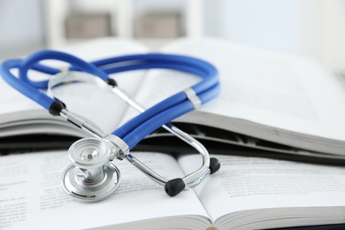 Photo of One medical stethoscope and books on table, closeup