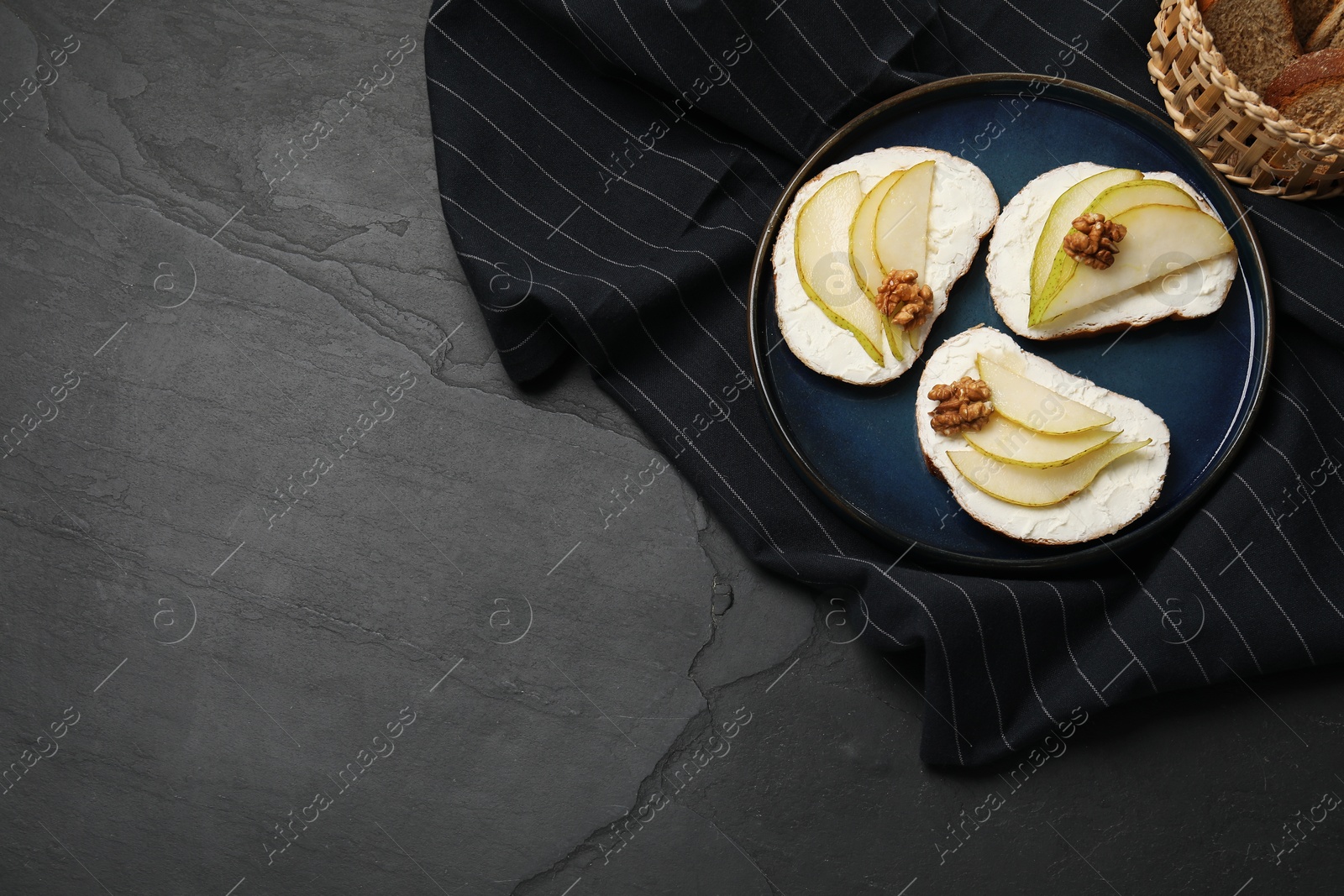 Photo of Delicious bruschettas with ricotta cheese, pears and walnuts on dark textured table, top view. Space for text