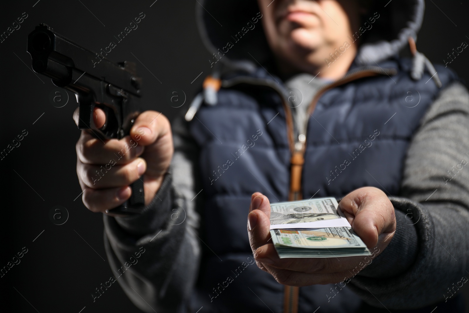 Photo of Dangerous criminal with gun holding money on black background, selective focus. Armed robbery