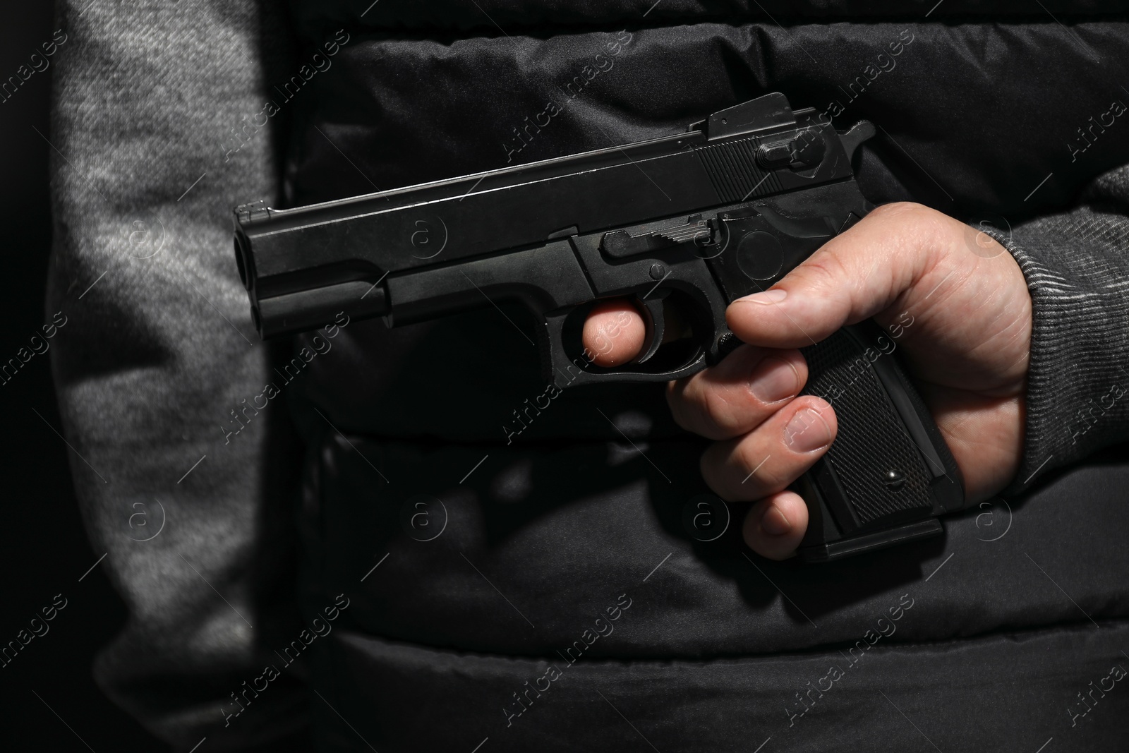 Photo of Man hiding gun behind his back on black background, closeup. Armed robbery