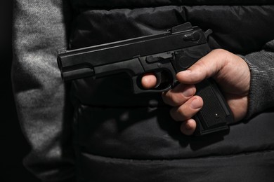 Man hiding gun behind his back on black background, closeup. Armed robbery