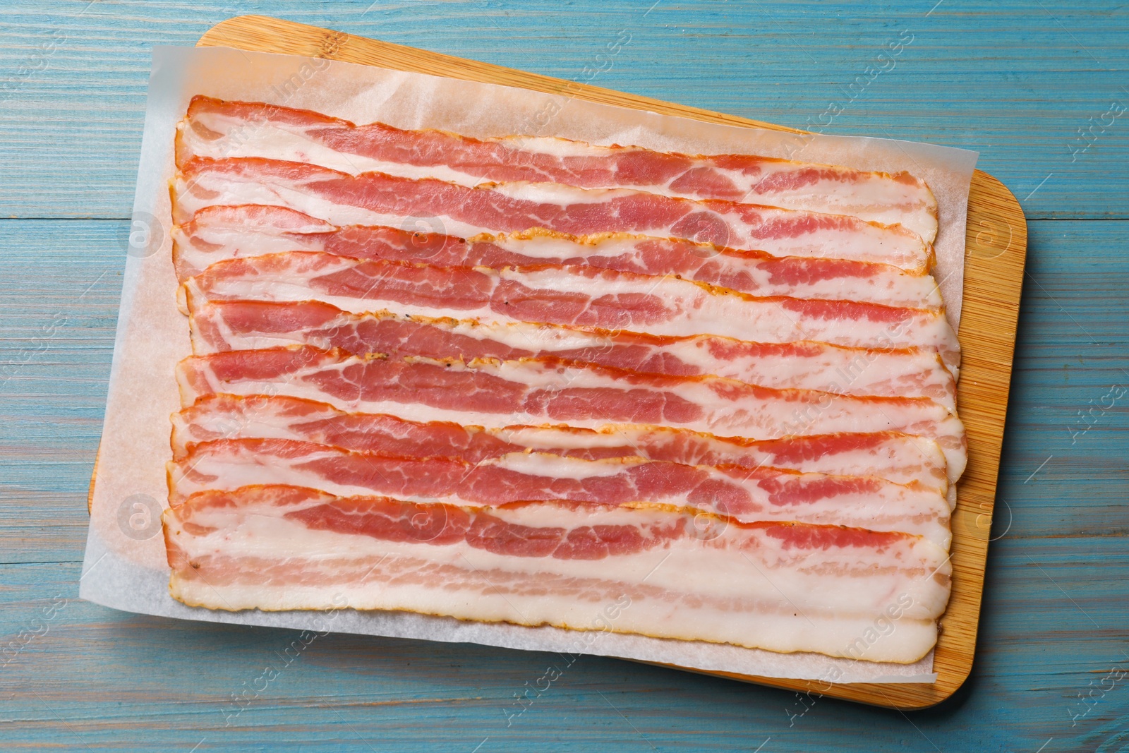 Photo of Slices of raw bacon on light blue wooden table, top view