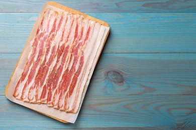 Photo of Slices of raw bacon on light blue wooden table, top view. Space for text