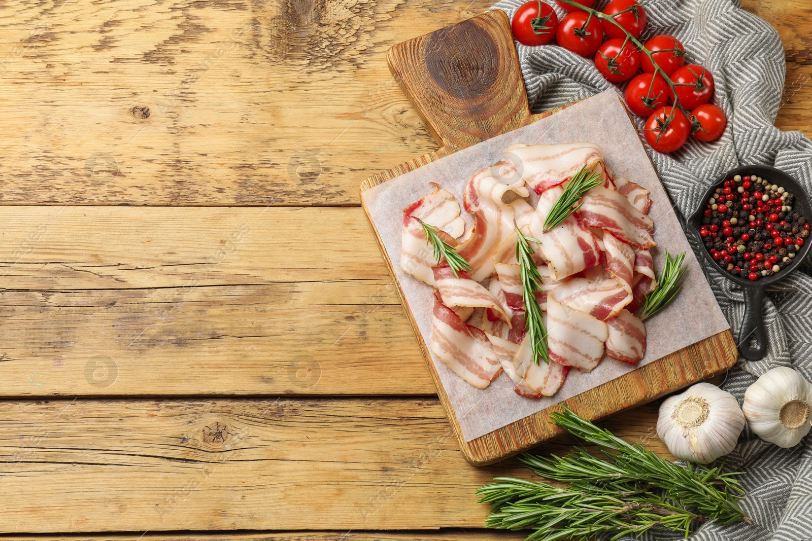 Photo of Slices of raw bacon, spices and tomatoes on wooden table, flat lay. Space for text