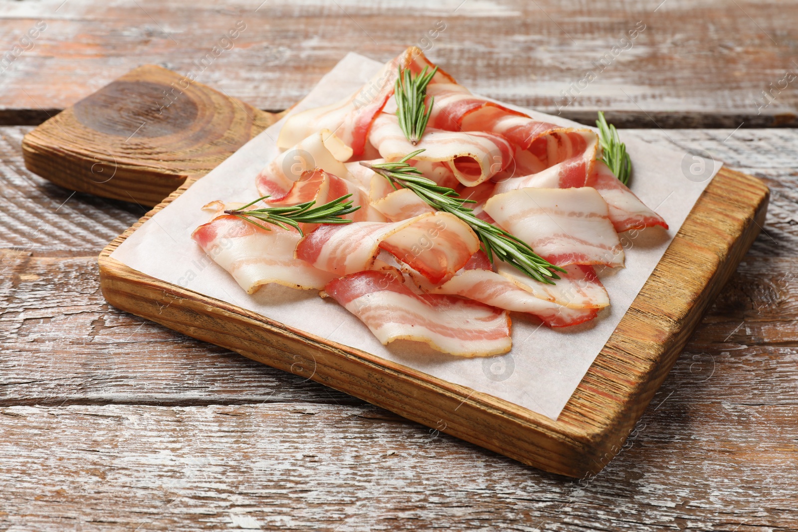 Photo of Slices of raw bacon and rosemary on wooden table