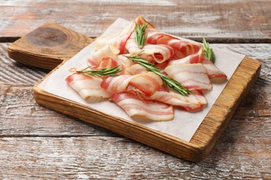 Slices of raw bacon and rosemary on wooden table