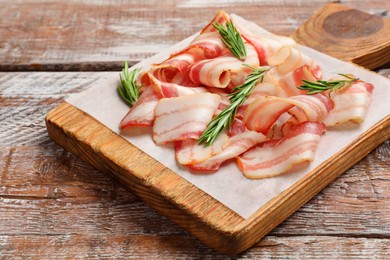 Slices of raw bacon and rosemary on wooden table