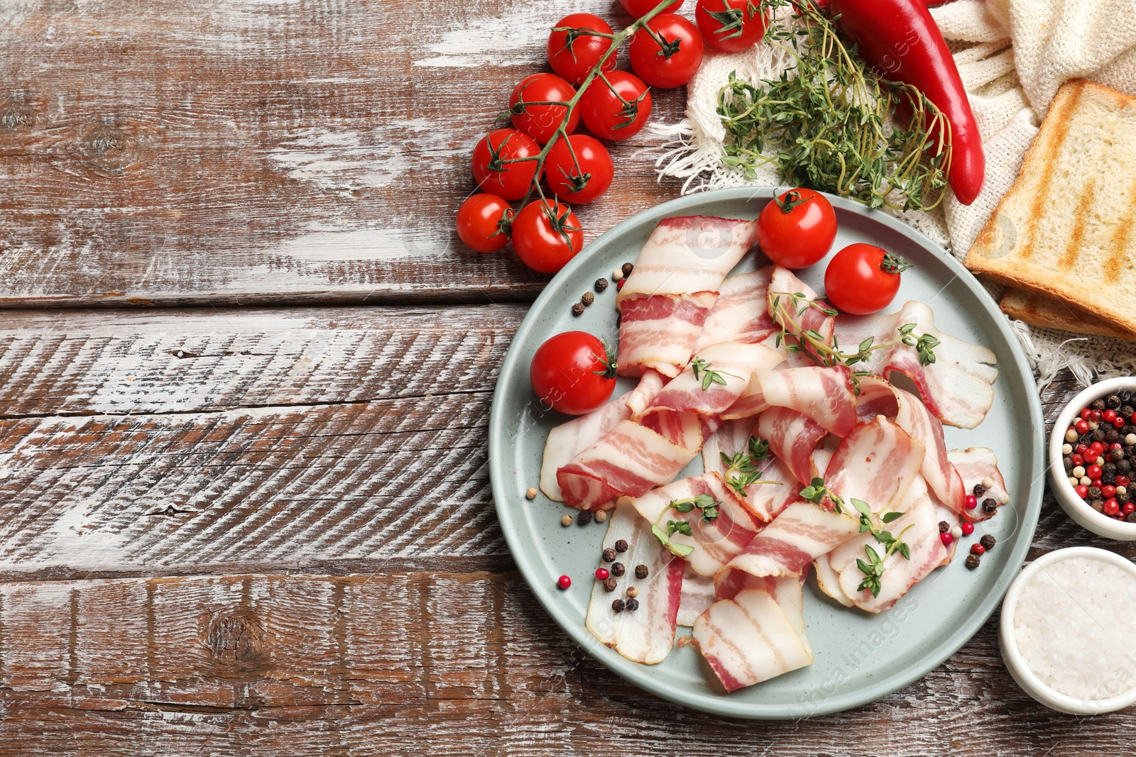 Photo of Slices of raw bacon, spices, bread and tomatoes on wooden table, flat lay. Space for text