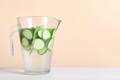 Photo of Refreshing cucumber water with rosemary in jug on white table against beige background. Space for text