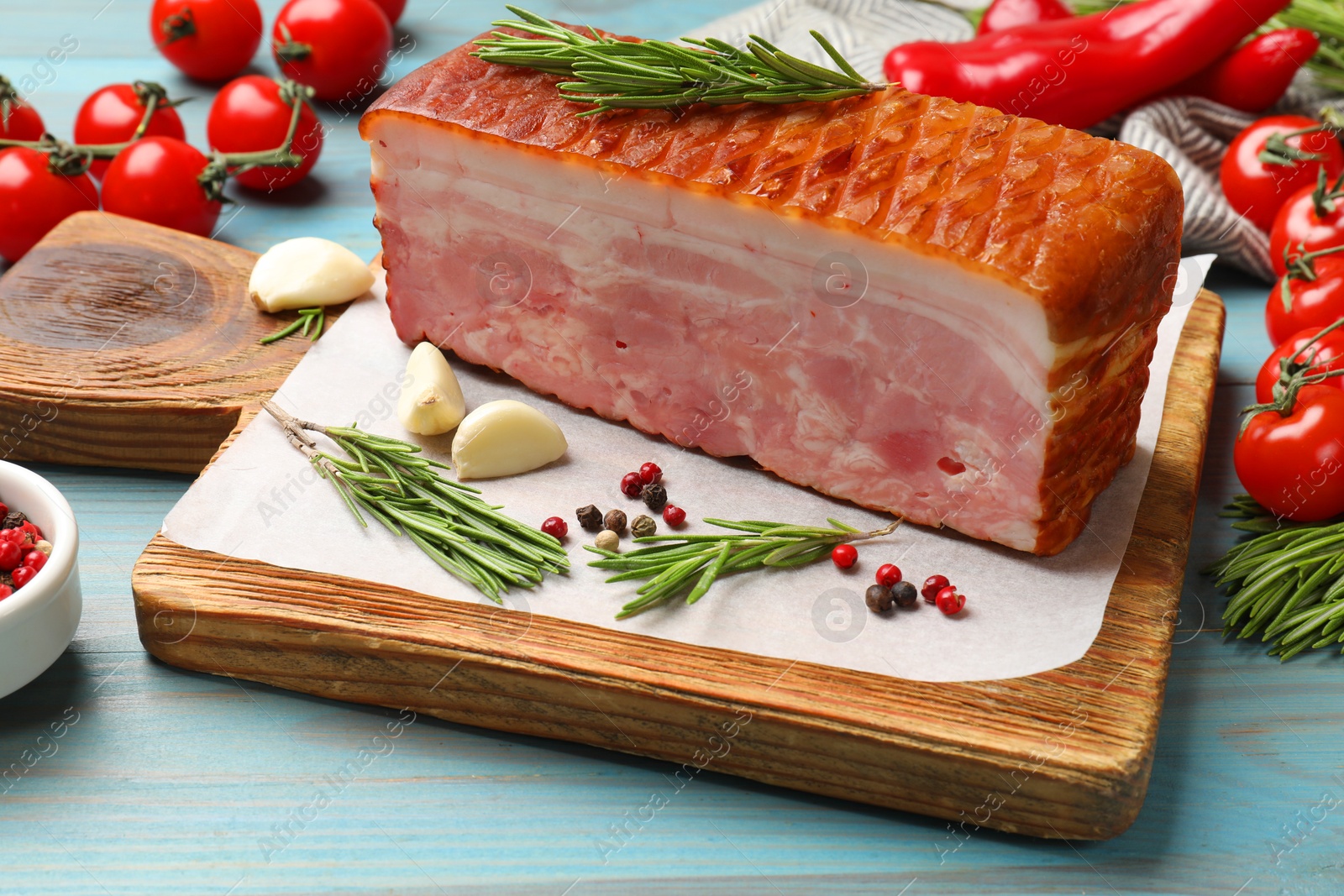 Photo of Piece of raw bacon with spices and cherry tomatoes on light blue wooden table