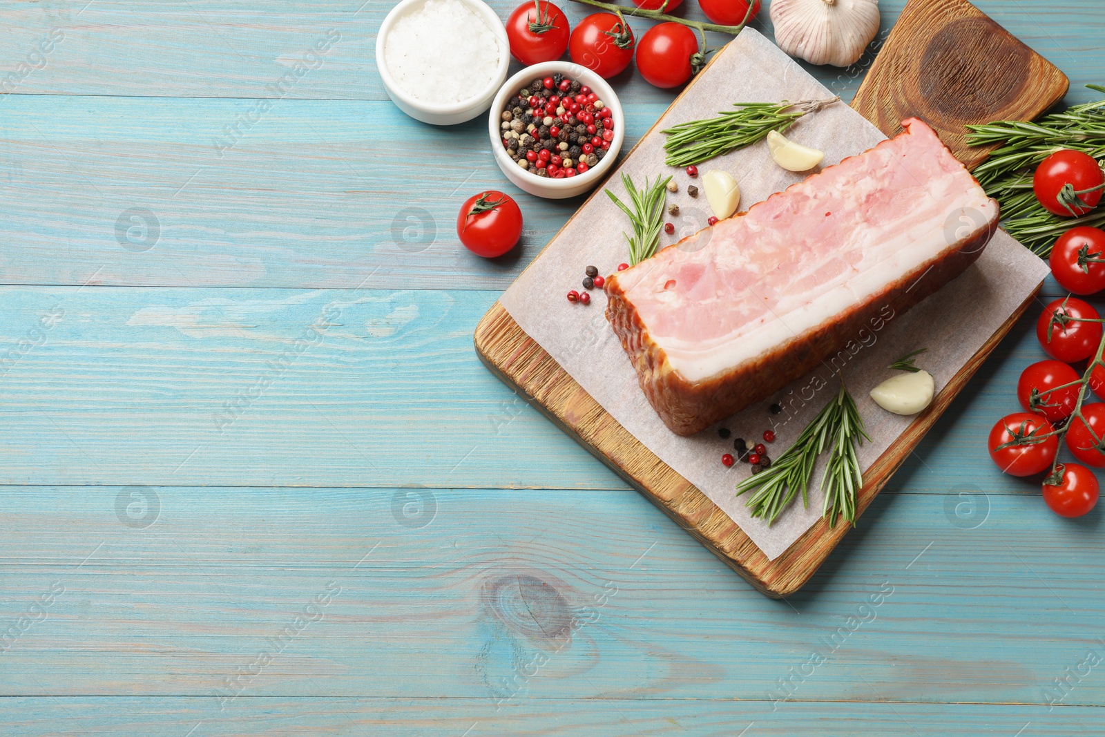 Photo of Piece of raw bacon with spices and tomatoes on light blue wooden table, flat lay. Space for text