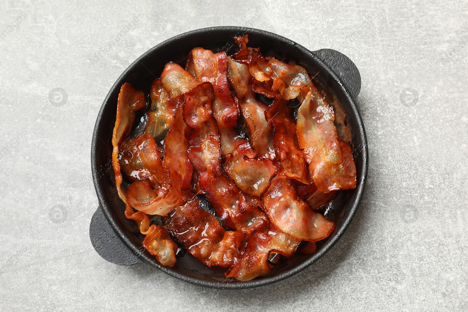 Photo of Delicious bacon slices in frying pan on light grey table, top view