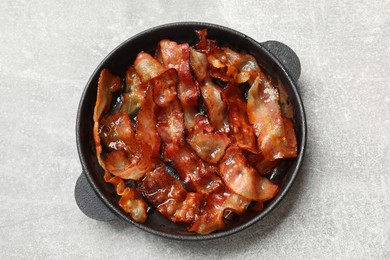 Delicious bacon slices in frying pan on light grey table, top view