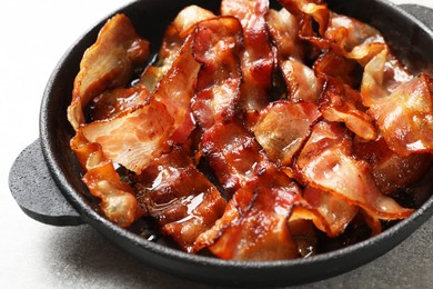 Delicious bacon slices in frying pan on light grey table, closeup