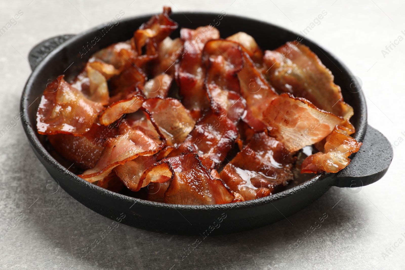 Photo of Delicious bacon slices in frying pan on light grey table, closeup