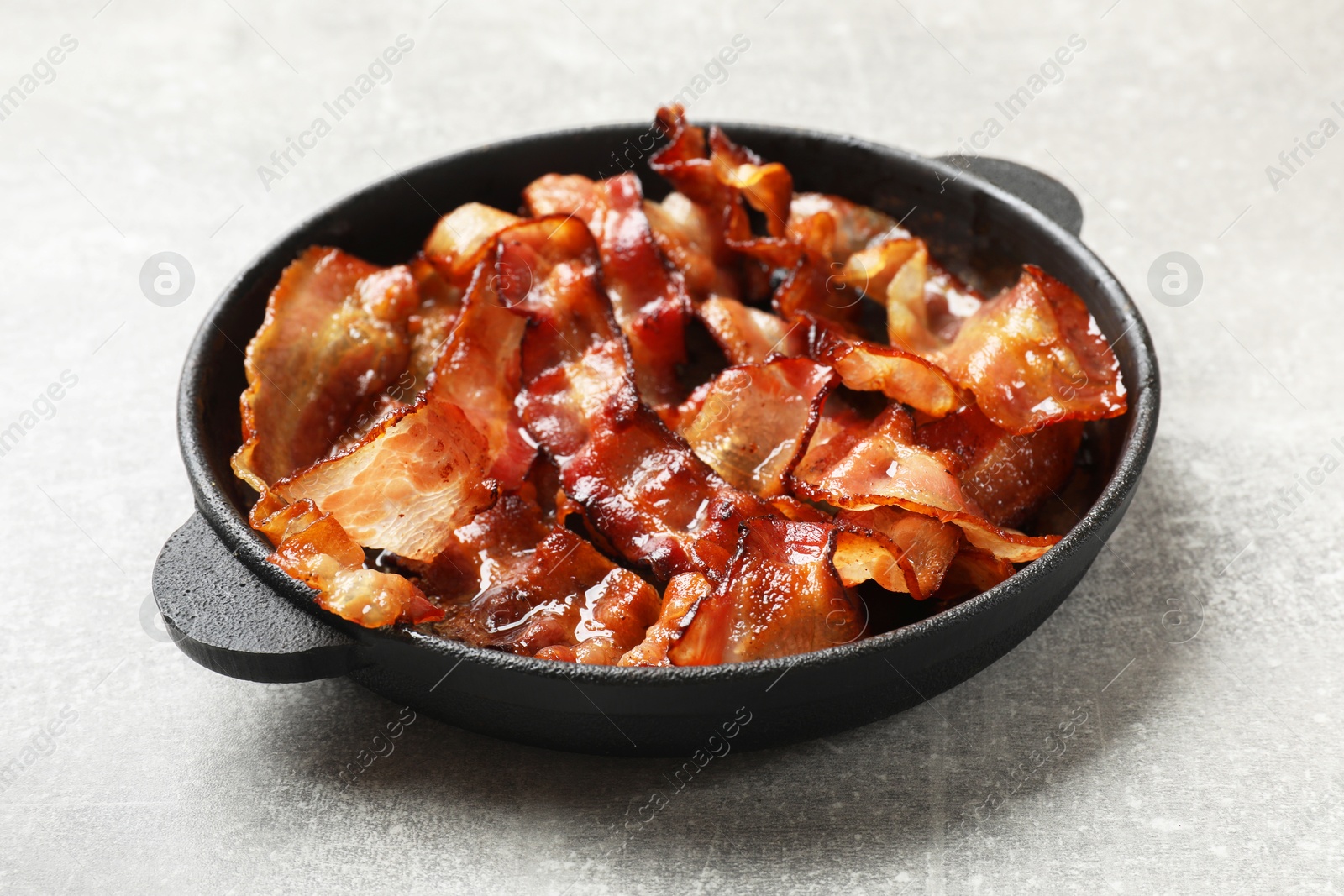 Photo of Delicious bacon slices in frying pan on light grey table