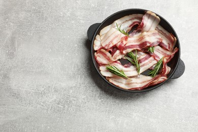 Photo of Delicious bacon slices and fresh rosemary in frying pan on light grey table, top view. Space for text