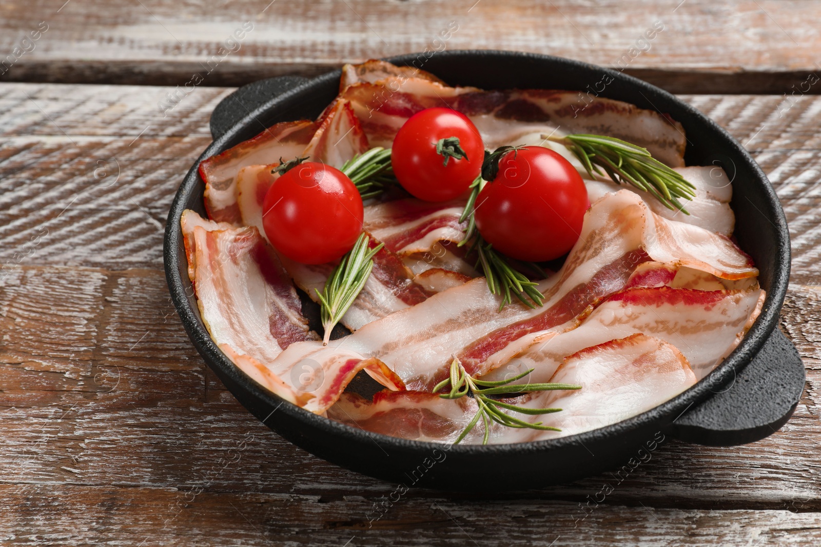 Photo of Delicious bacon slices, spices and cherry tomatoes in frying pan on wooden table