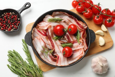 Photo of Delicious bacon slices in frying pan, spices and tomatoes on white table, flat lay