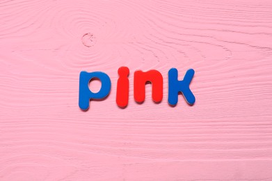 Word Pink made of magnetic letters on bright wooden background, top view. Learning alphabet