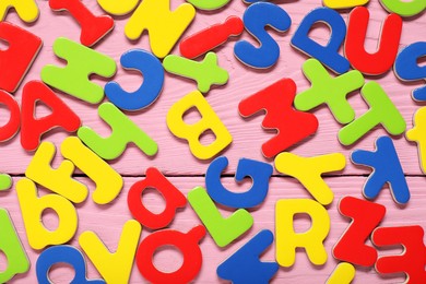 Photo of Learning alphabet. Magnetic letters on pink wooden background, flat lay