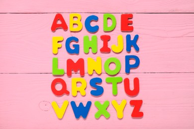 Alphabetical order. Bright magnetic letters on pink wooden background, top view